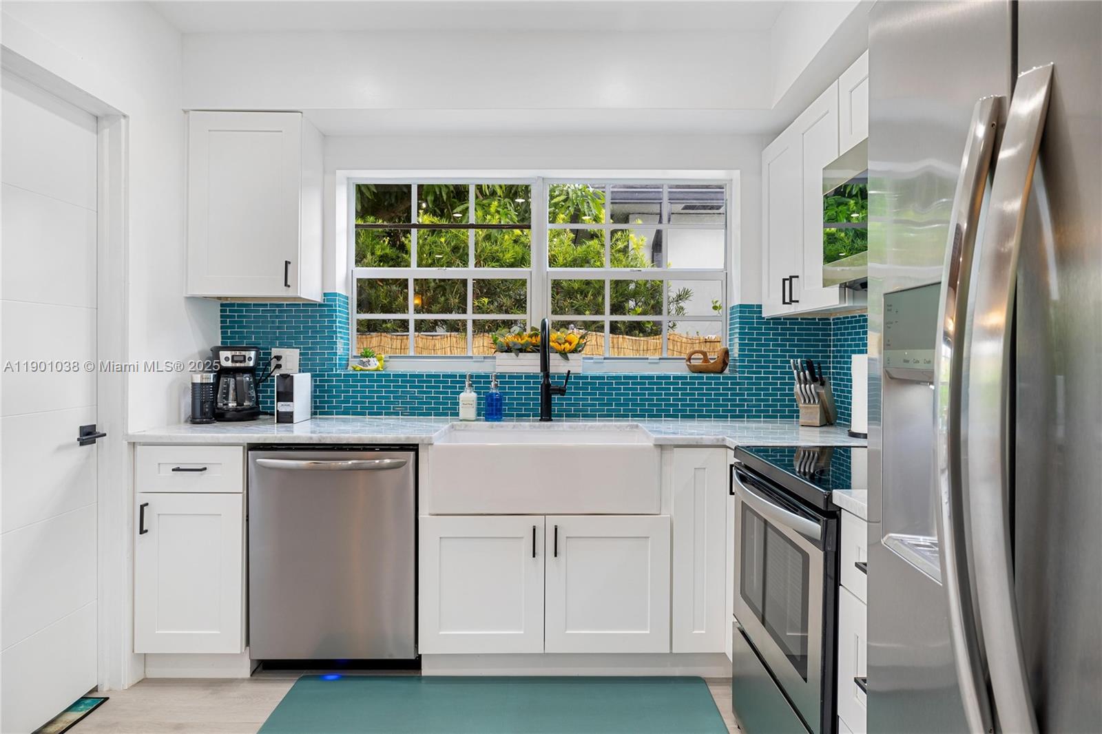 A kitchen features white cabinets, a farmhouse sink, stainless steel appliances, and a teal backsplash — 8926 Abbott Ave # 0, Surfside FL 33154, SURFSIDE, FL