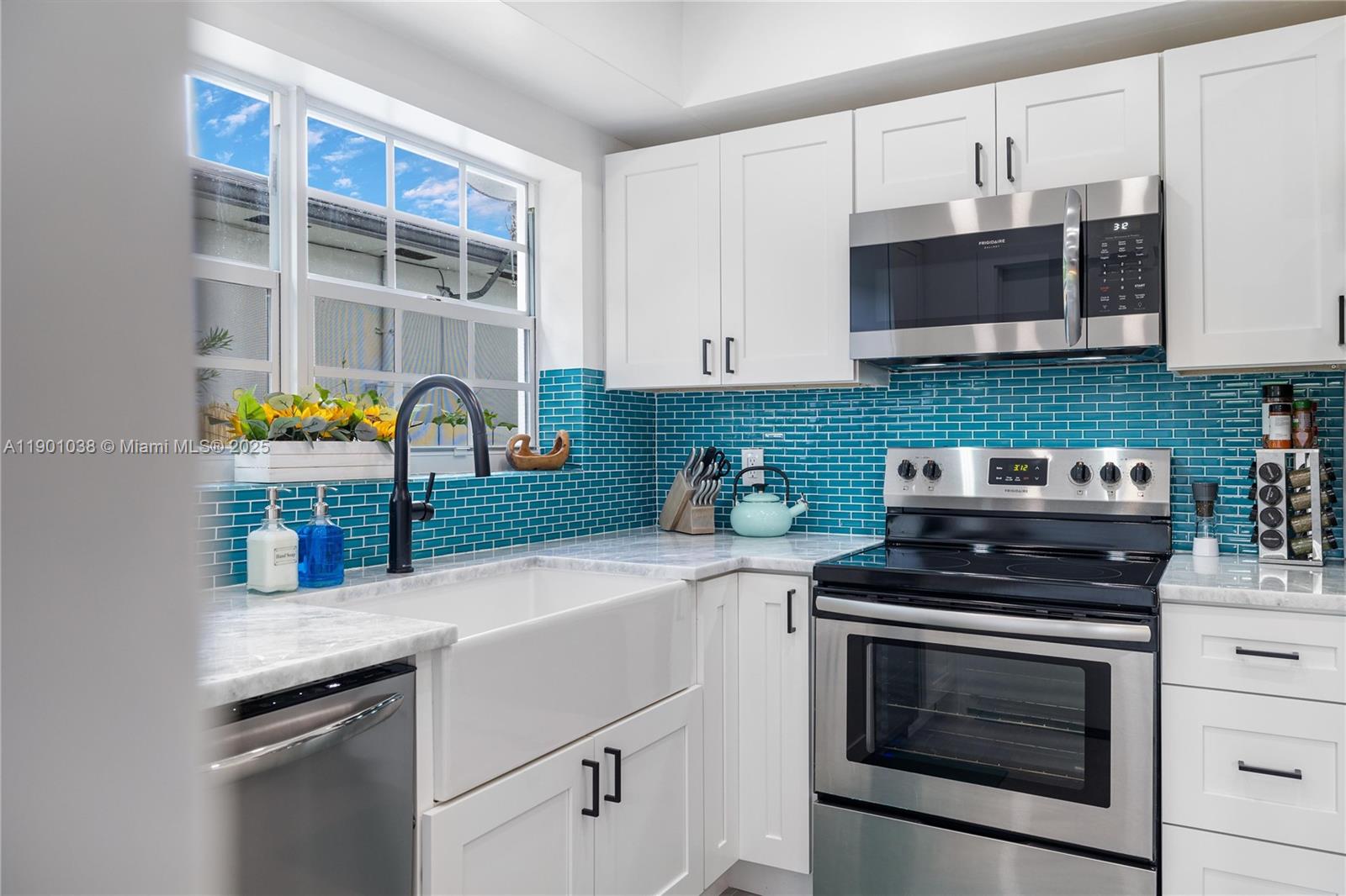 A kitchen features white cabinets, a farmhouse sink, stainless steel appliances, and a teal backsplash — 8926 Abbott Ave # 0, Surfside FL 33154, SURFSIDE, FL