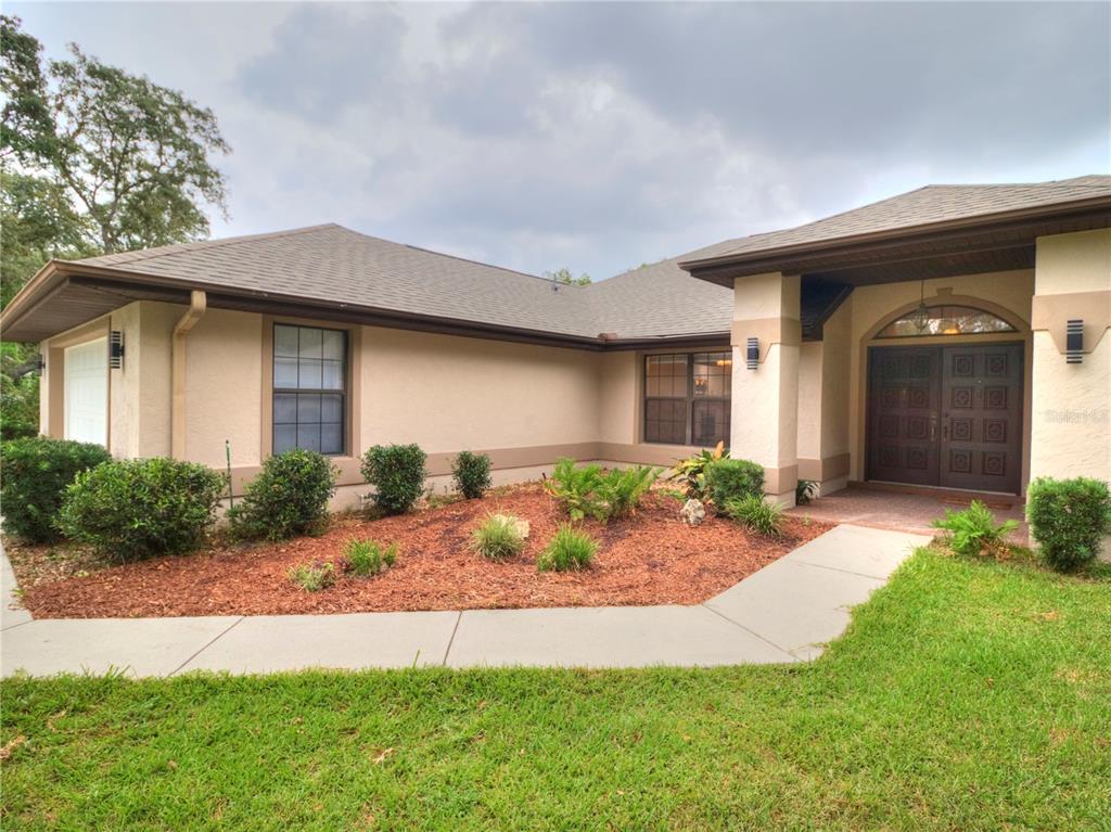 The exterior of a single-story house features a tan stucco facade, brown roof, and landscaping — 5360 SW 86TH LANE, OCALA, FL