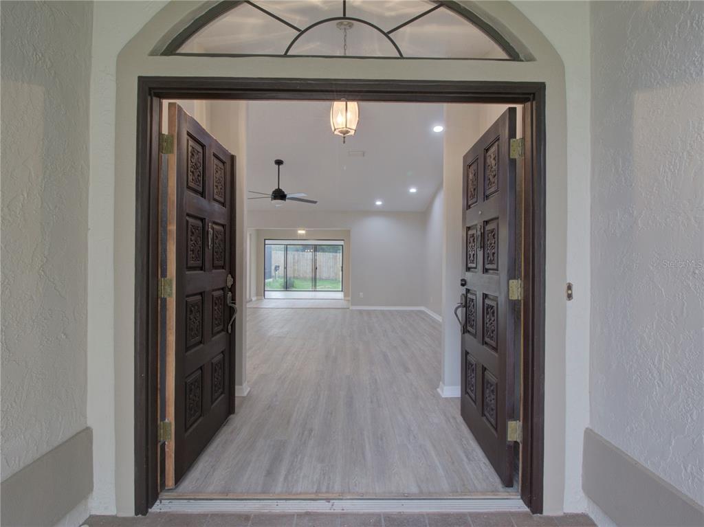 An open double door reveals a living room with light wood-look flooring and a ceiling fan — 5360 SW 86TH LANE, OCALA, FL