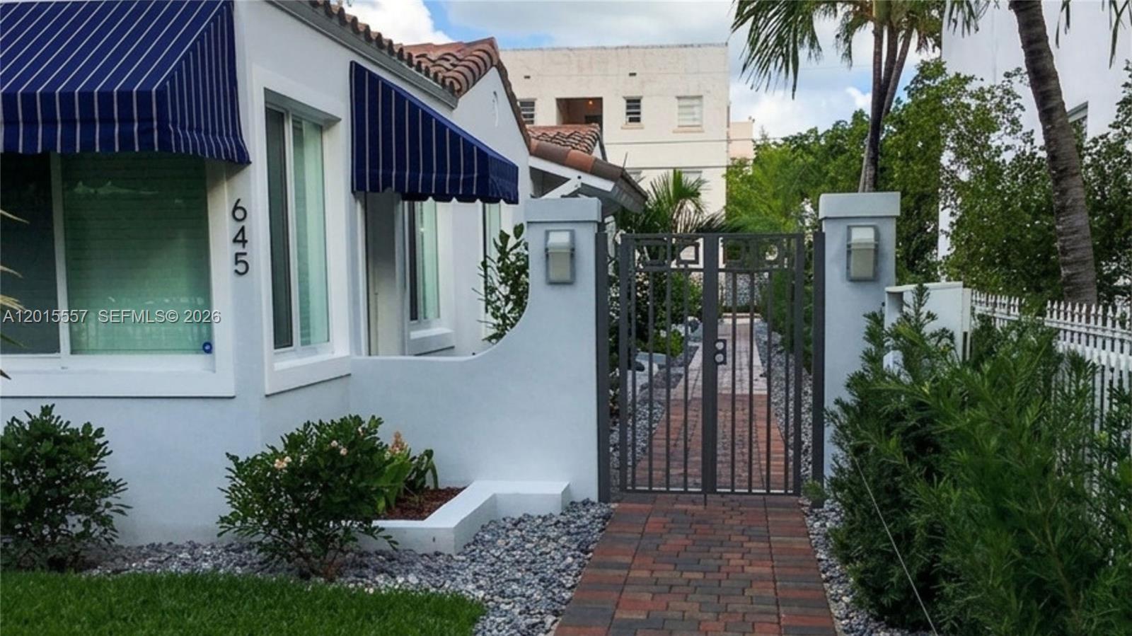 A white house with blue striped awnings features a brick walkway leading to a gated entrance — 645 Lenox Ave, Miami Beach FL 33139, MIAMI BEACH, FL
