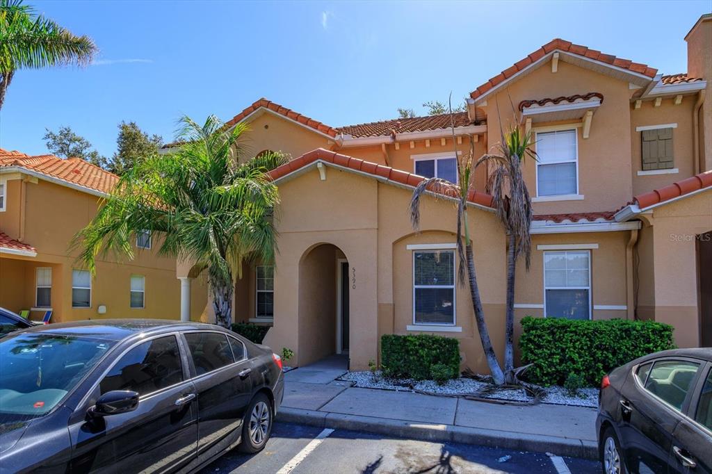 A two-story tan stucco townhouse with a tile roof and a palm tree out front — 5390 PARADISE CAY CIRCLE, KISSIMMEE, FL