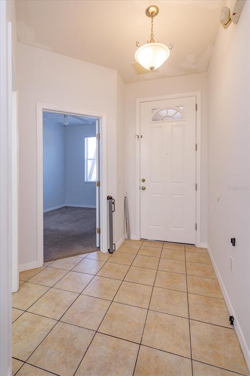 An entryway with tan tile flooring, a white front door, and a doorway to a bedroom — 5390 PARADISE CAY CIRCLE, KISSIMMEE, FL