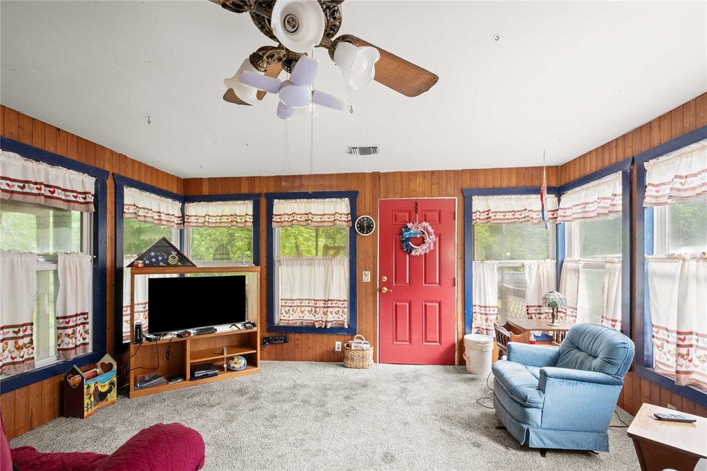 A sunroom with wood-paneled walls, gray carpeting, a red door, and a ceiling fan — 14702 CR 719, WEBSTER, FL