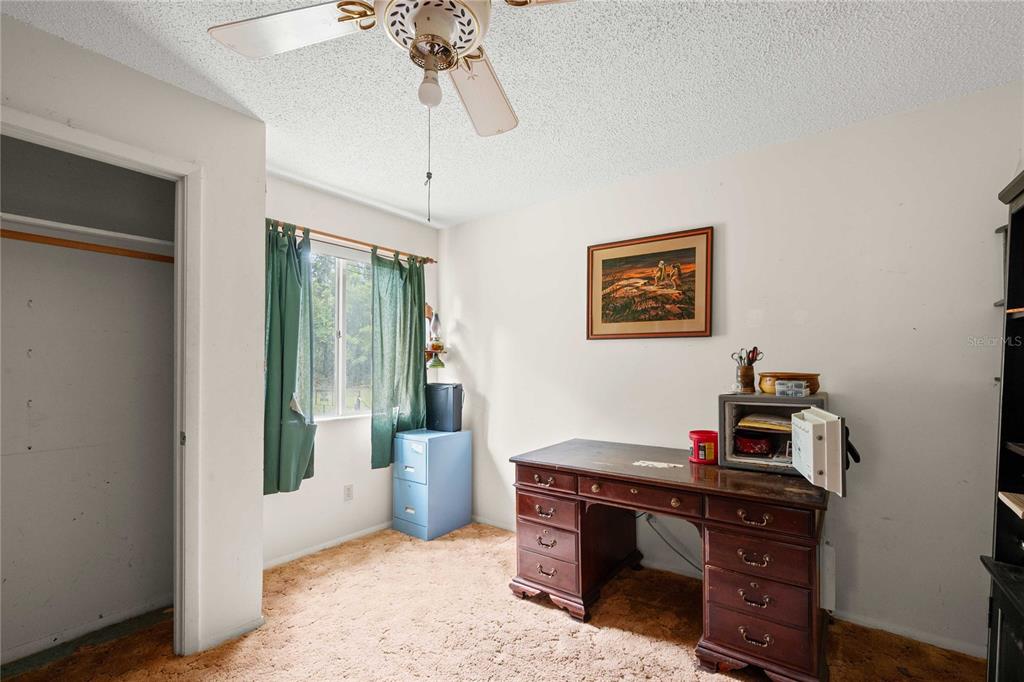 A bedroom features tan carpet, a wooden desk with an open safe, and a ceiling fan — 14702 CR 719, WEBSTER, FL