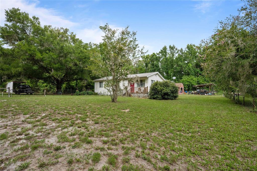 A single-story house with white siding sits on a large, grassy lot with trees — 14702 CR 719, WEBSTER, FL