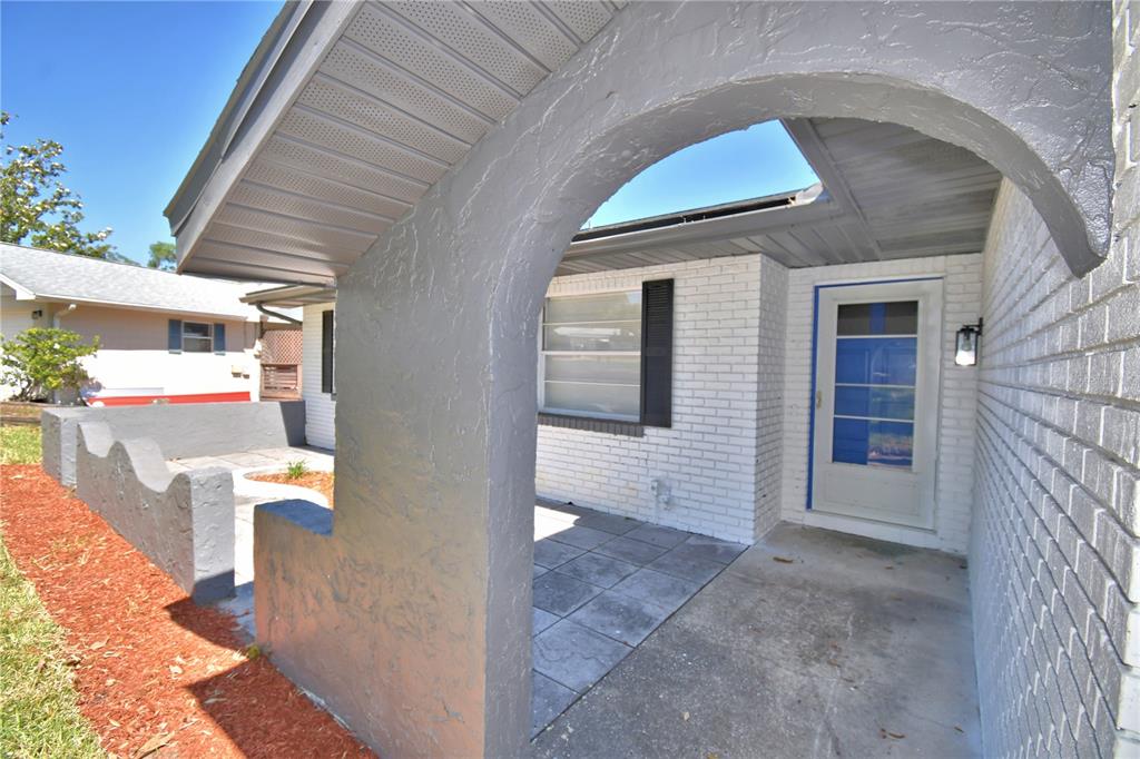 A gray arched entryway leads to a white brick house with a tiled porch — 138 WHITTIER LANE, WINTER HAVEN, FL