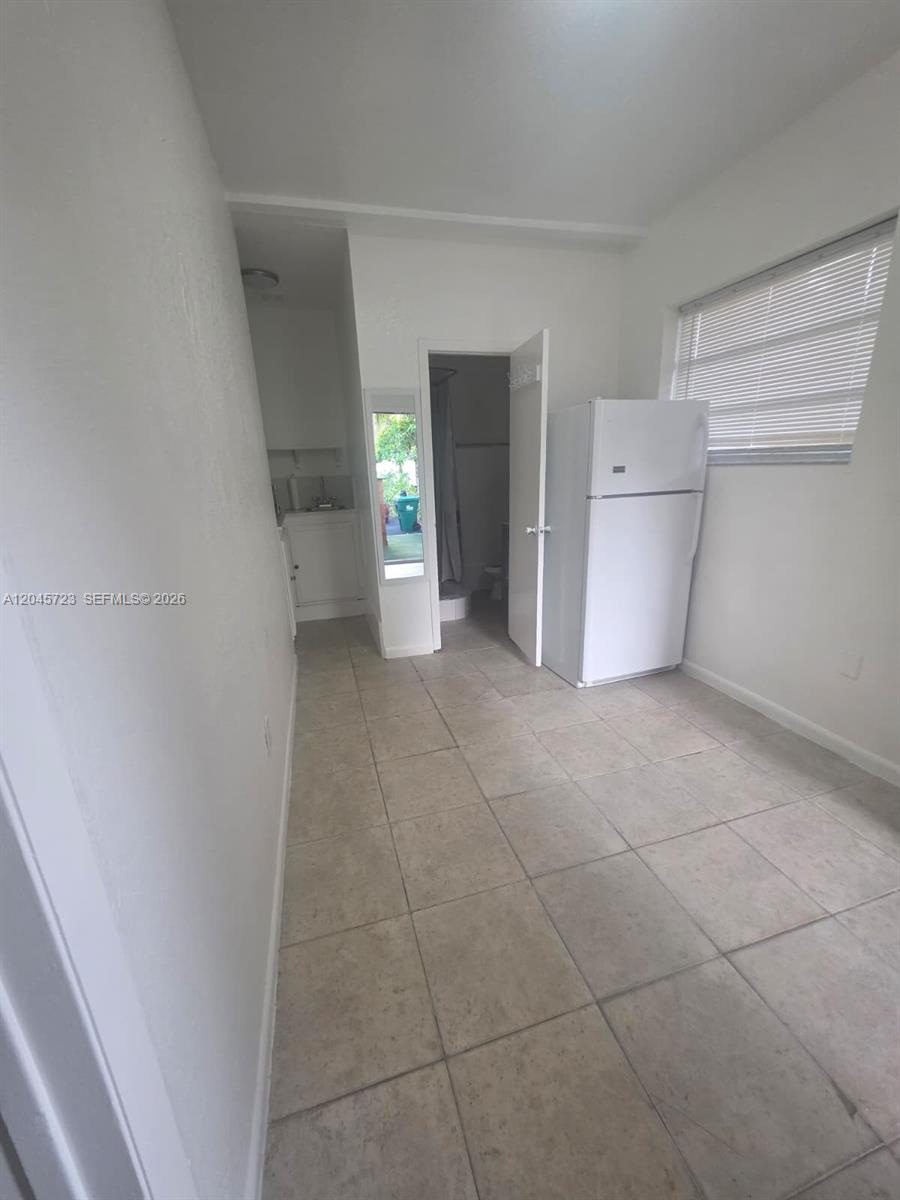 A small room features white walls, tile flooring, a white refrigerator, and a bathroom doorway — 10861 NW 22nd Ct # 0, Miami FL 33167, MIAMI, FL