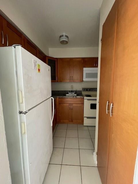 A galley kitchen features wood cabinets, white appliances, and light-colored tile flooring — 1711 S Cypress Road, Pompano Beach FL 33060, POMPANO BEACH, FL