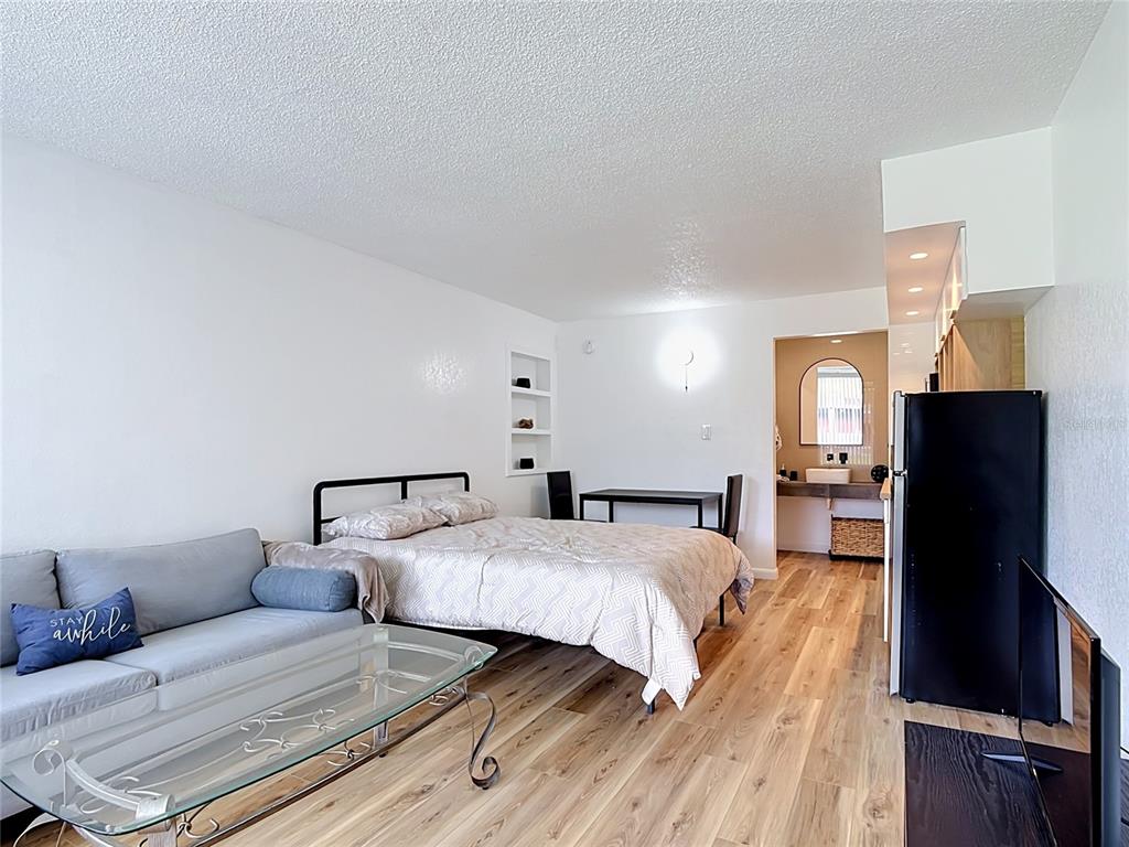 A studio apartment features a sofa, bed, dining table, and an open bathroom vanity area — 43420 HIGHWAY 27 UNIT 320, DAVENPORT, FL
