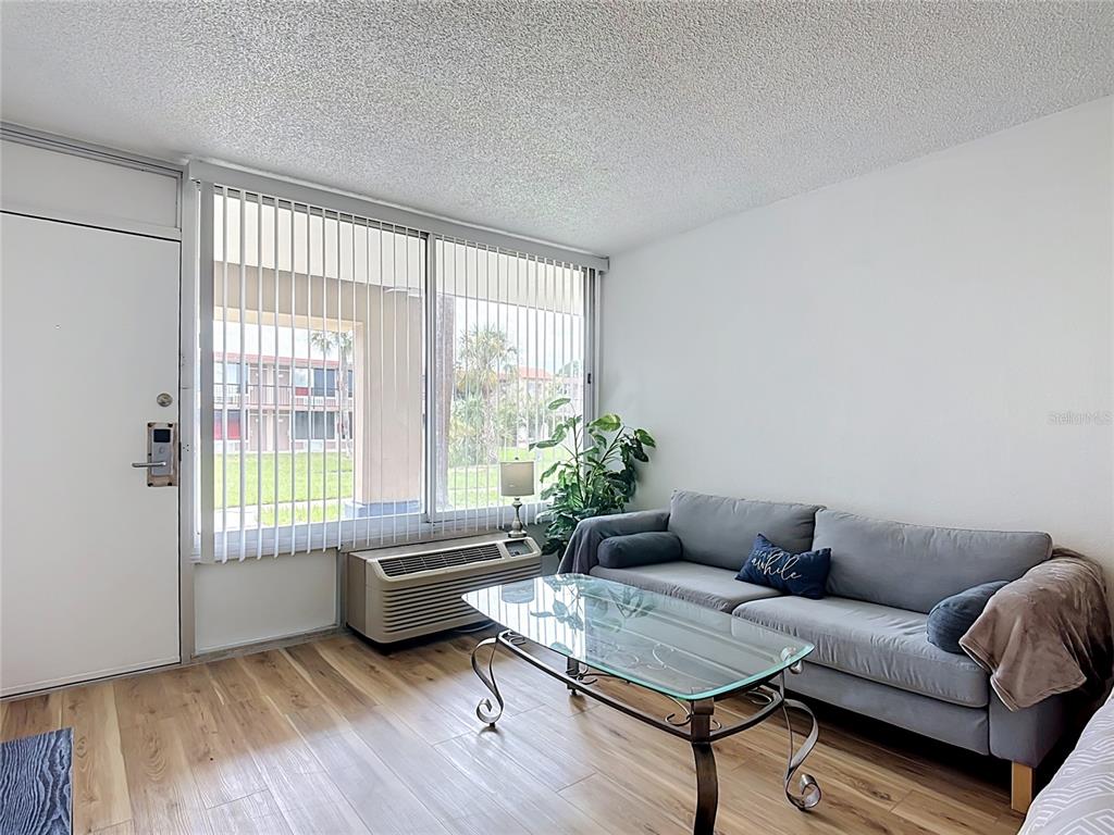 A living room features light wood-look flooring, a grey sofa, a glass coffee table, and blinds — 43420 HIGHWAY 27 UNIT 320, DAVENPORT, FL
