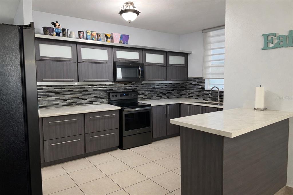 A kitchen features dark wood cabinetry, a black appliance suite, and a tiled backsplash — 2623 CALLE PALMA DE SIERRA, PONCE, PR