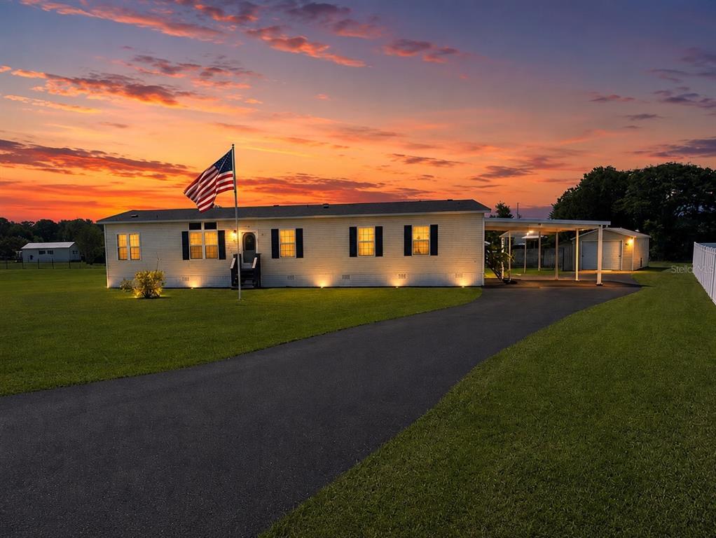 A single-story house with a driveway, carport, and American flag at sunset — 13718 COUNTY ROAD 109D-3, LADY LAKE, FL