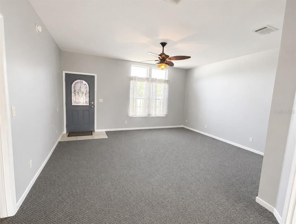 A living room features gray carpet, light gray walls, a ceiling fan, and a front door — 13718 COUNTY ROAD 109D-3, LADY LAKE, FL