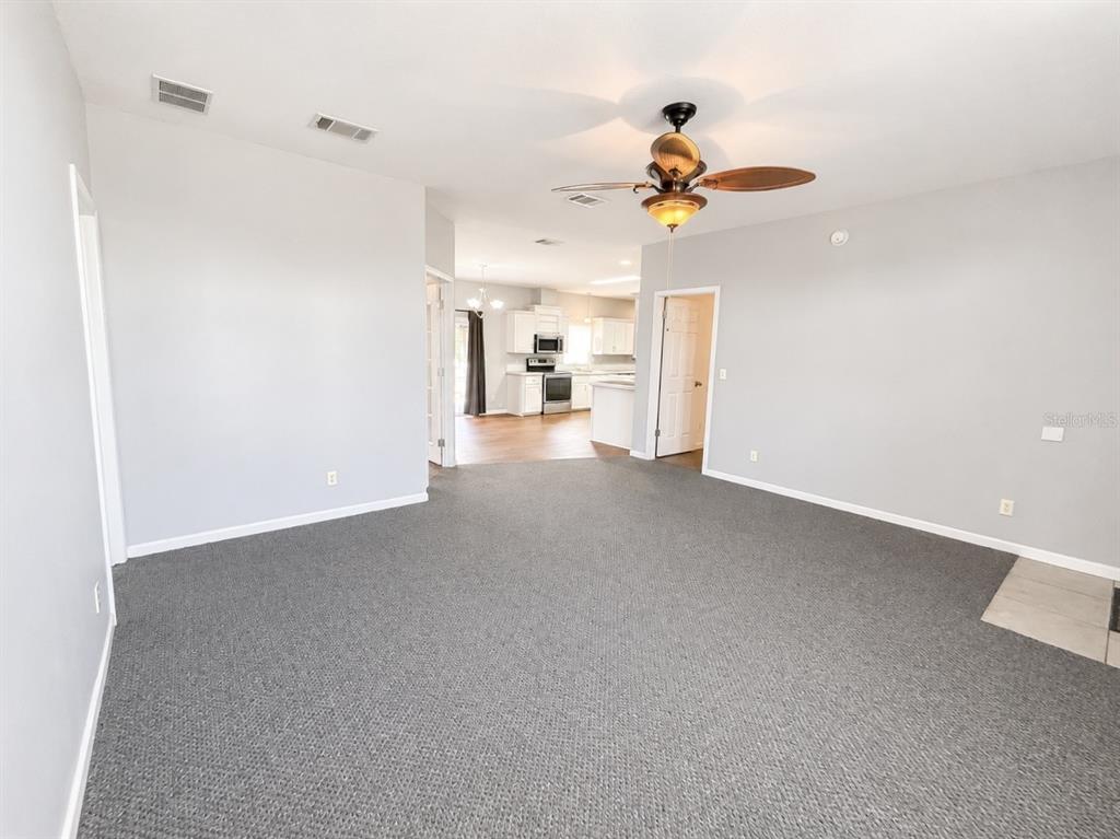 A carpeted living room leads to an open kitchen with white cabinets and wood flooring — 13718 COUNTY ROAD 109D-3, LADY LAKE, FL