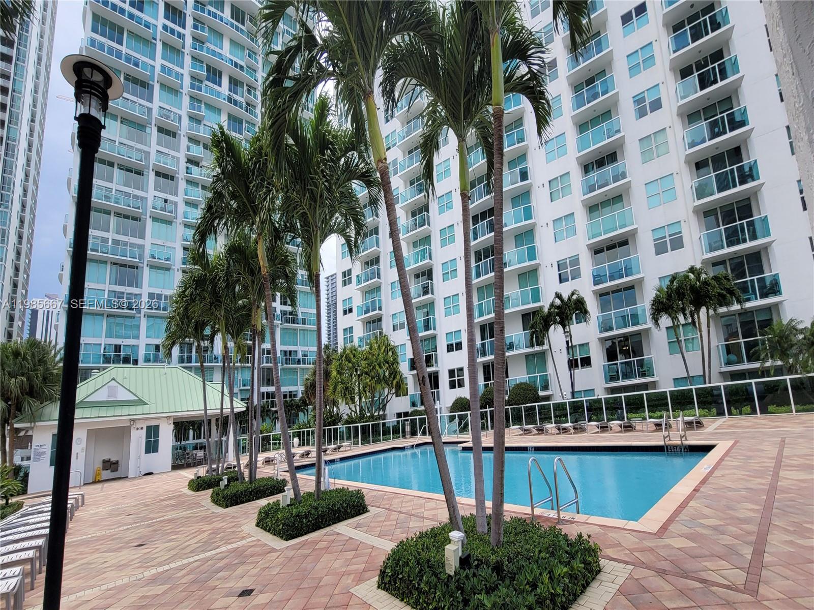 A swimming pool sits on a paved deck surrounded by palm trees and high-rise buildings — 31 SE 5th St # 1110, Miami FL 33131, MIAMI, FL