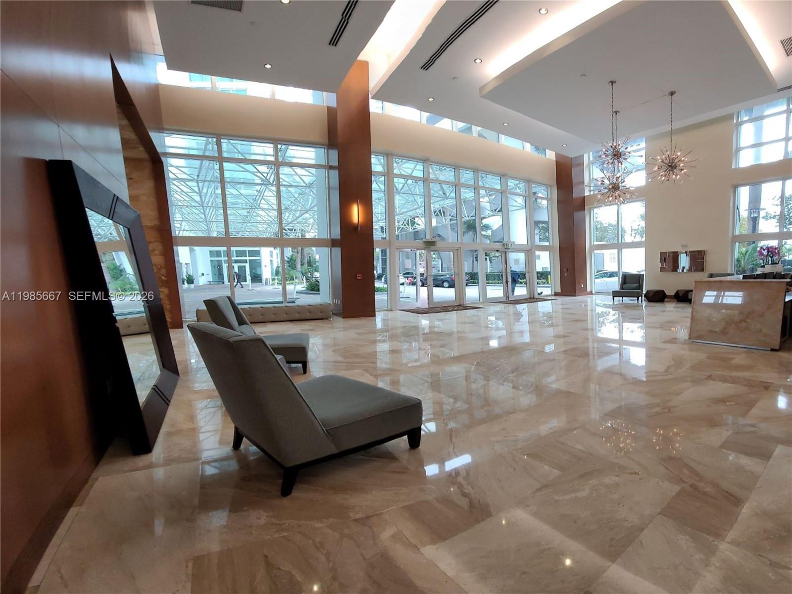 A spacious, modern lobby features high ceilings, marble floors, floor-to-ceiling windows, and contemporary seating — 31 SE 5th St # 1110, Miami FL 33131, MIAMI, FL
