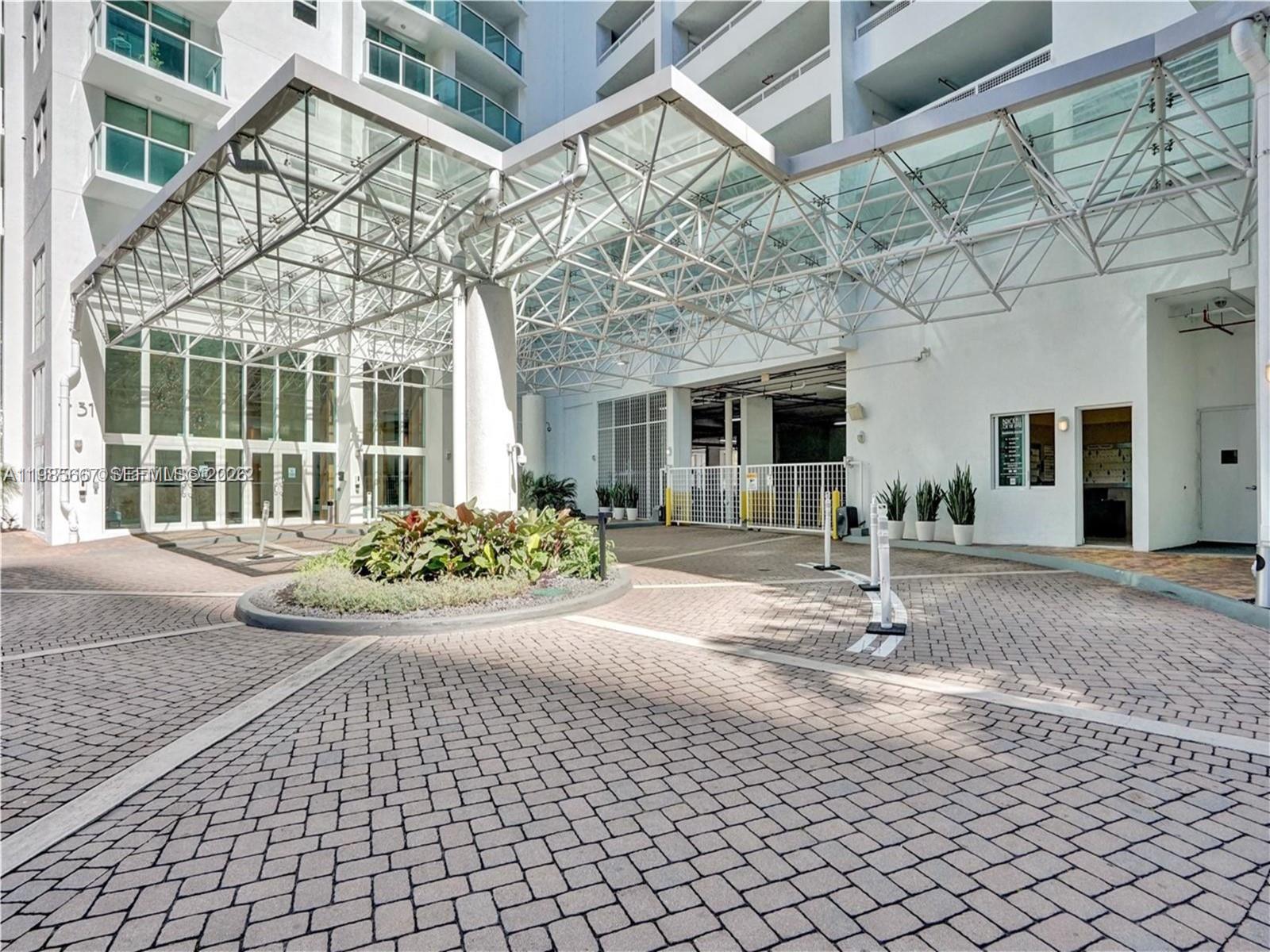 A paved driveway leads to the glass-covered entrance of a modern multi-story residential building — 31 SE 5th St # 1110, Miami FL 33131, MIAMI, FL