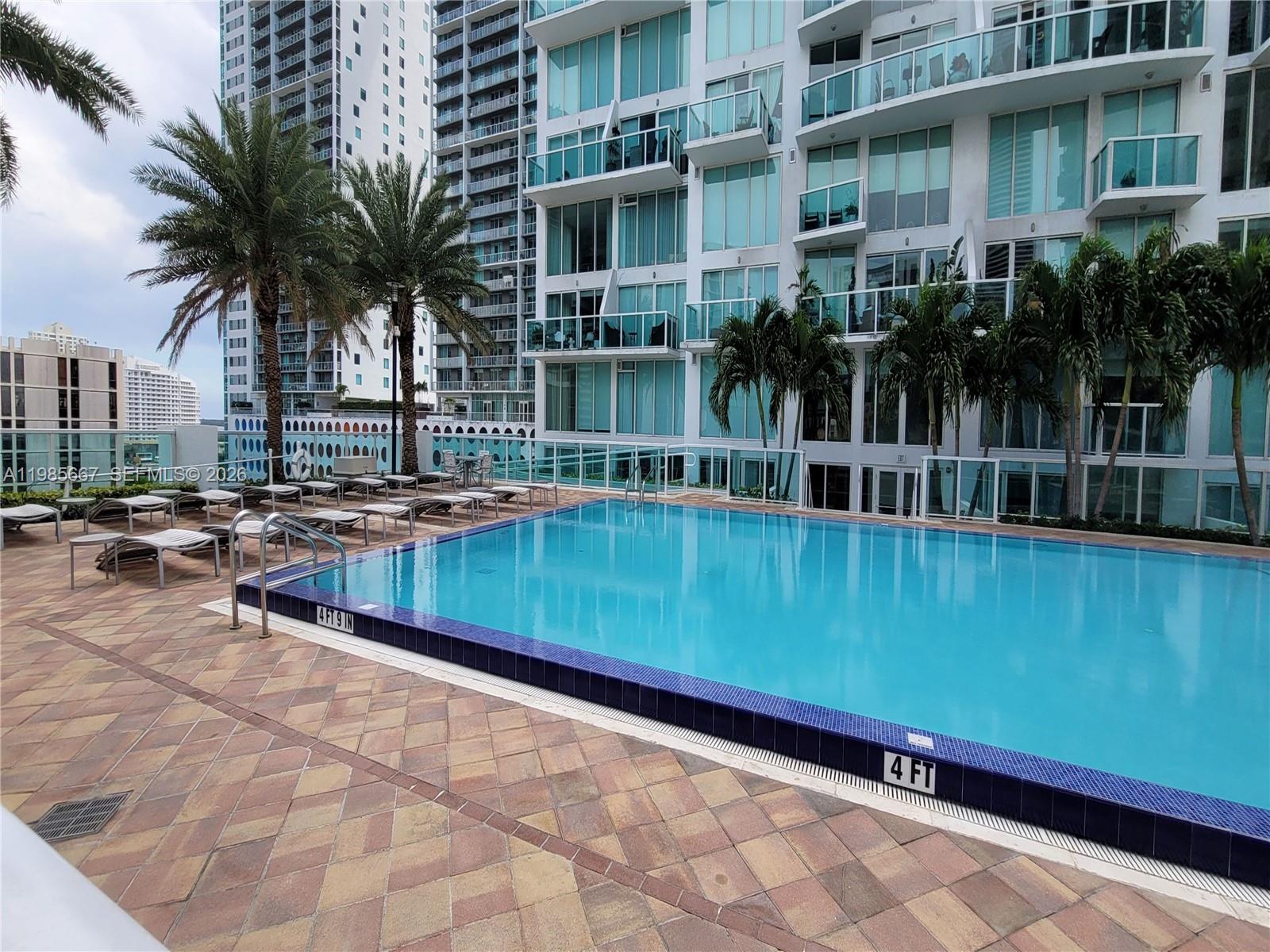 A swimming pool with blue tiles sits on a paved deck beside a modern building — 31 SE 5th St # 1110, Miami FL 33131, MIAMI, FL