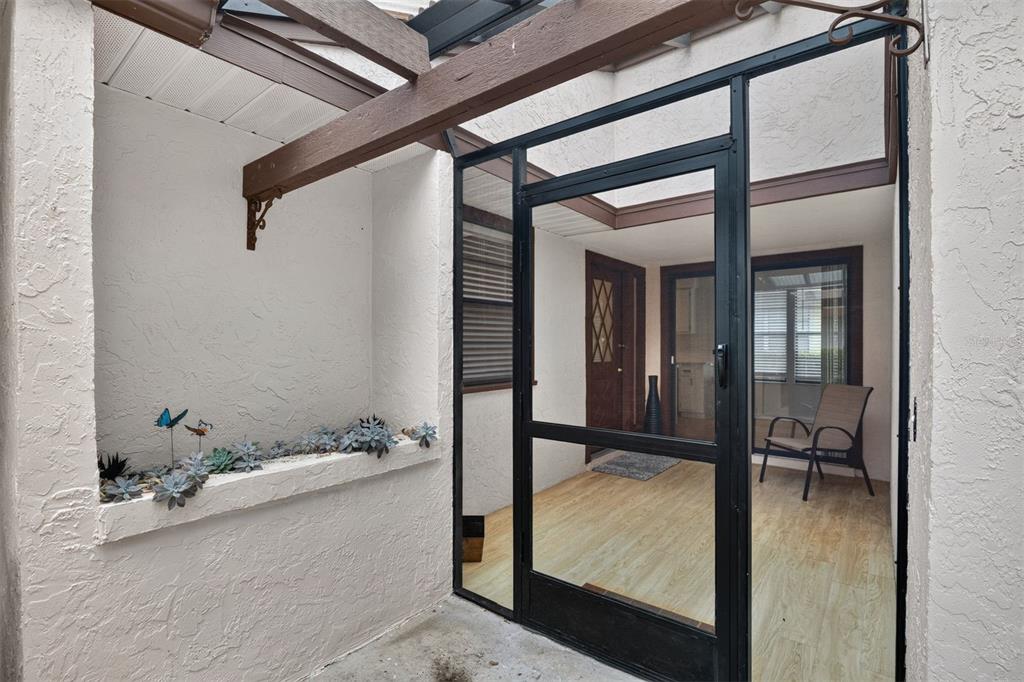 A screened-in entryway features a wood-look floor, a built-in planter, and a wooden beam overhead — 8391 NW 39TH CIRCLE, GAINESVILLE, FL