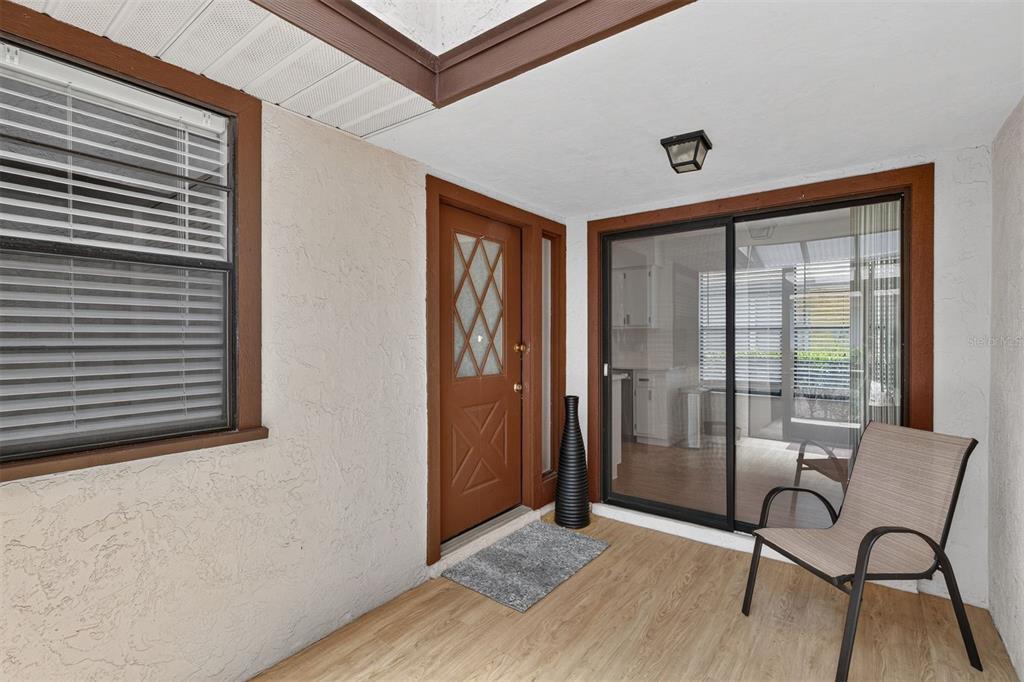 A covered patio features wood-look flooring, a brown front door, and a sliding glass door — 8391 NW 39TH CIRCLE, GAINESVILLE, FL