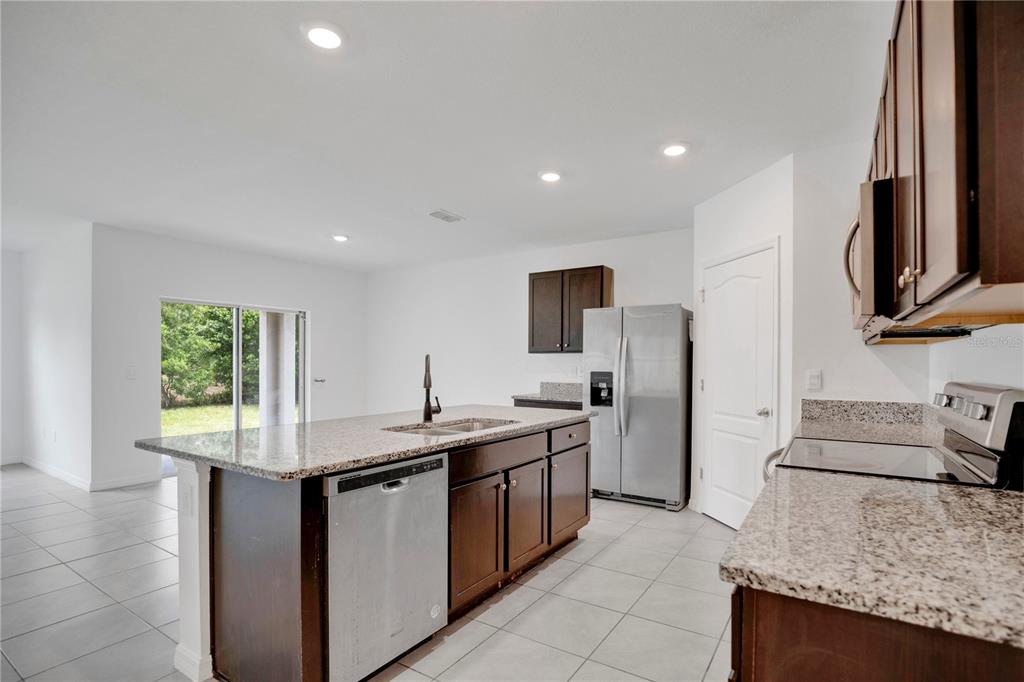 A kitchen features dark wood cabinets, granite countertops, stainless steel appliances, and tile flooring — 1942 MARLOW STREET, DELTONA, FL