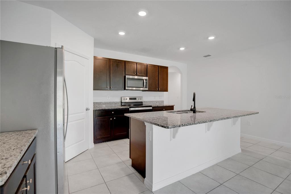 A kitchen features dark wood cabinets, granite countertops, a center island, and tile flooring — 1942 MARLOW STREET, DELTONA, FL