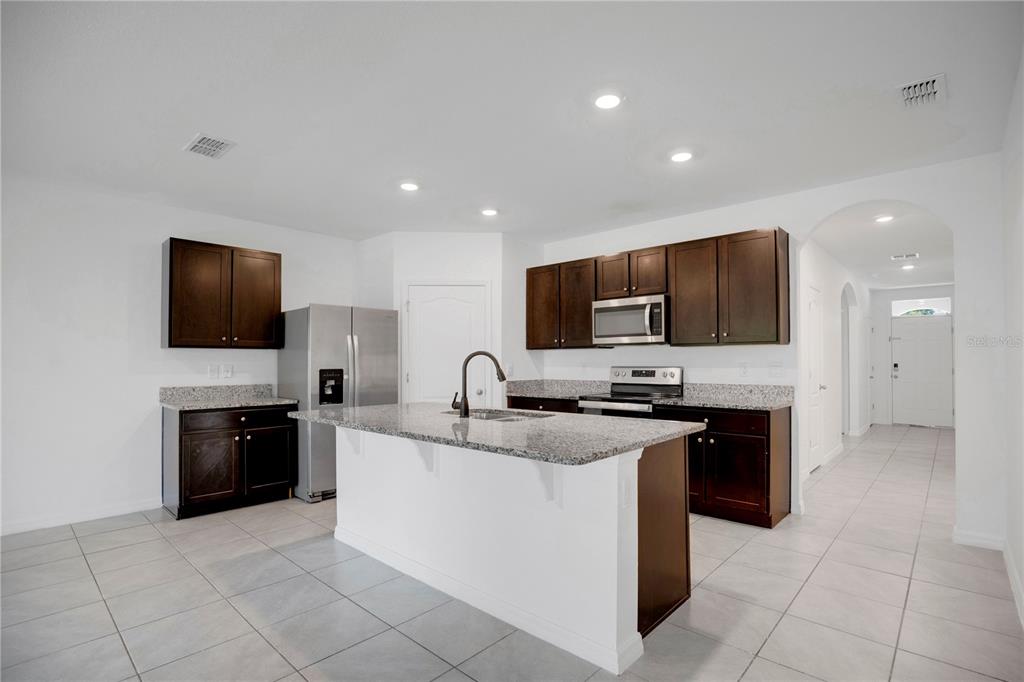 A kitchen features dark wood cabinets, granite countertops, a center island, and light tile flooring — 1942 MARLOW STREET, DELTONA, FL
