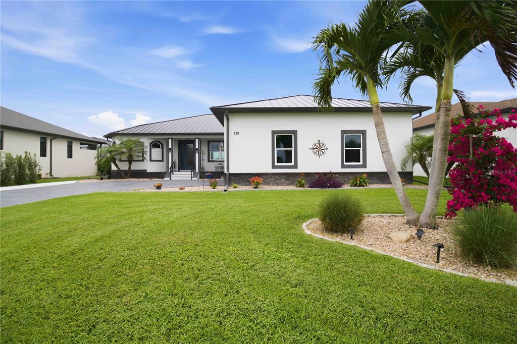 A single-story house with a white exterior, dark metal roof, and a manicured front lawn — 216 ROTONDA BOULEVARD E, ROTONDA WEST, FL