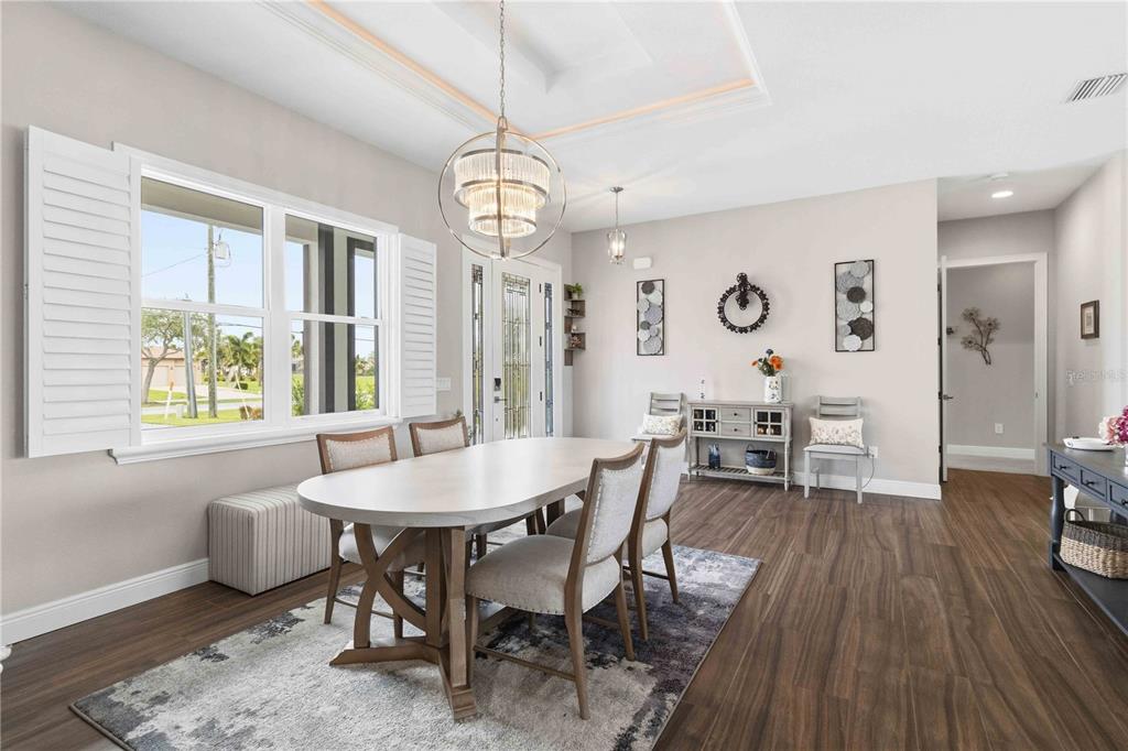 A dining room features a wooden table, upholstered chairs, a chandelier, and a large window — 216 ROTONDA BOULEVARD E, ROTONDA WEST, FL