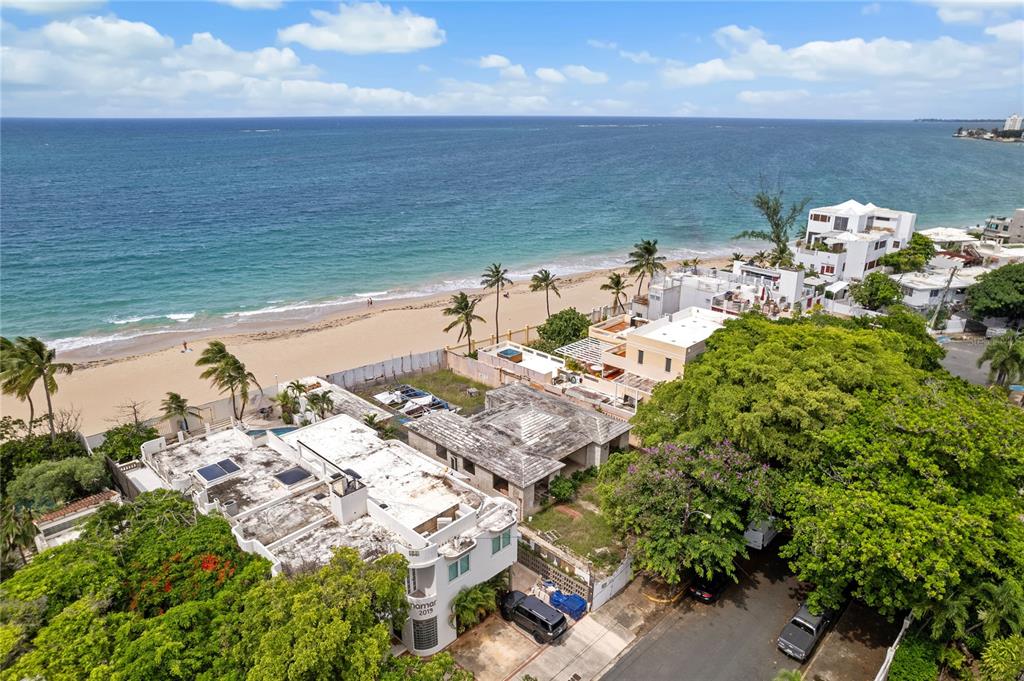 An aerial view shows a beachfront property with several buildings, palm trees, and a sandy beach — 2021 CALLE ITALIA, SAN JUAN, PR