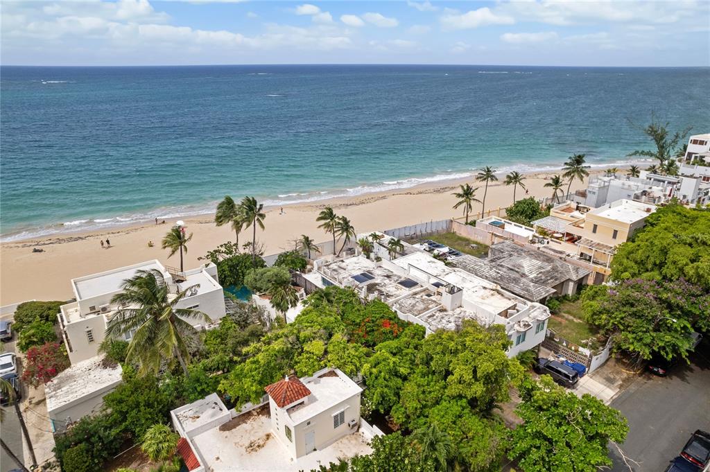 An aerial view shows beachfront houses with flat roofs, palm trees, and a sandy shore — 2021 CALLE ITALIA, SAN JUAN, PR