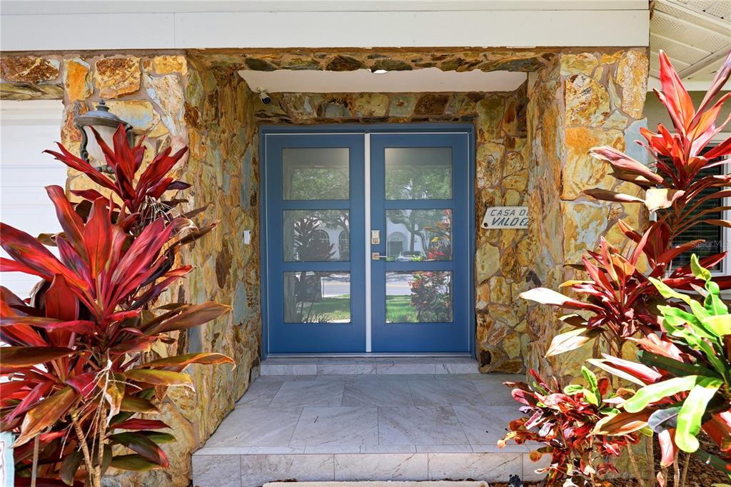 A blue double front door is set within a stone-clad entryway flanked by tropical plants — 13867 FEATHER SOUND DRIVE, CLEARWATER, FL