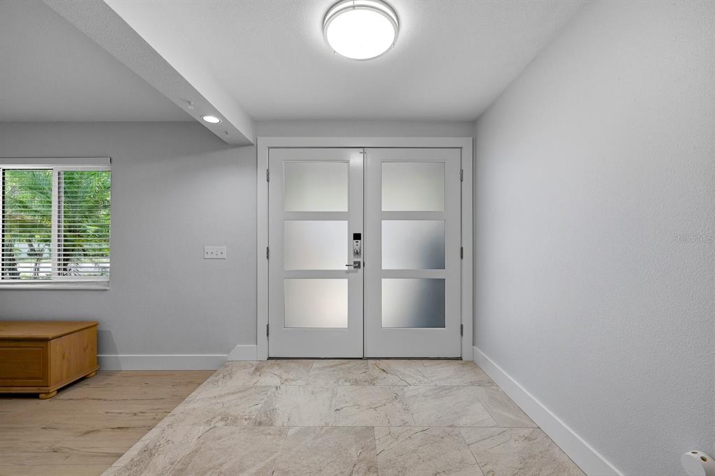 A bright entryway features double glass-paneled doors, light tile flooring, and a window with blinds — 13867 FEATHER SOUND DRIVE, CLEARWATER, FL