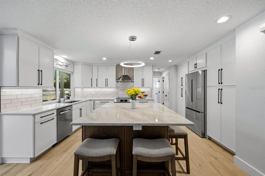 A modern kitchen features white cabinets, a large central island, and stainless steel appliances — 13867 FEATHER SOUND DRIVE, CLEARWATER, FL