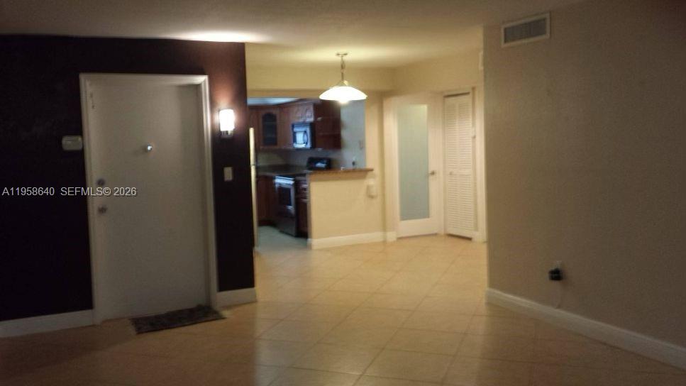 An interior view shows a tiled living area leading to a kitchen with wooden cabinets — 7368 SW 82nd St # E113, Miami FL 33143, MIAMI, FL