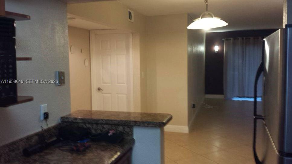 A kitchen counter overlooks a living area with tile flooring and a sliding glass door — 7368 SW 82nd St # E113, Miami FL 33143, MIAMI, FL