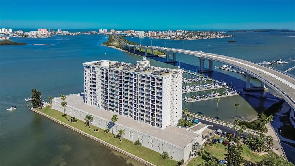 An aerial view shows a tall residential building situated on a waterfront lot near a bridge — 100 PIERCE STREET UNIT 703, CLEARWATER, FL