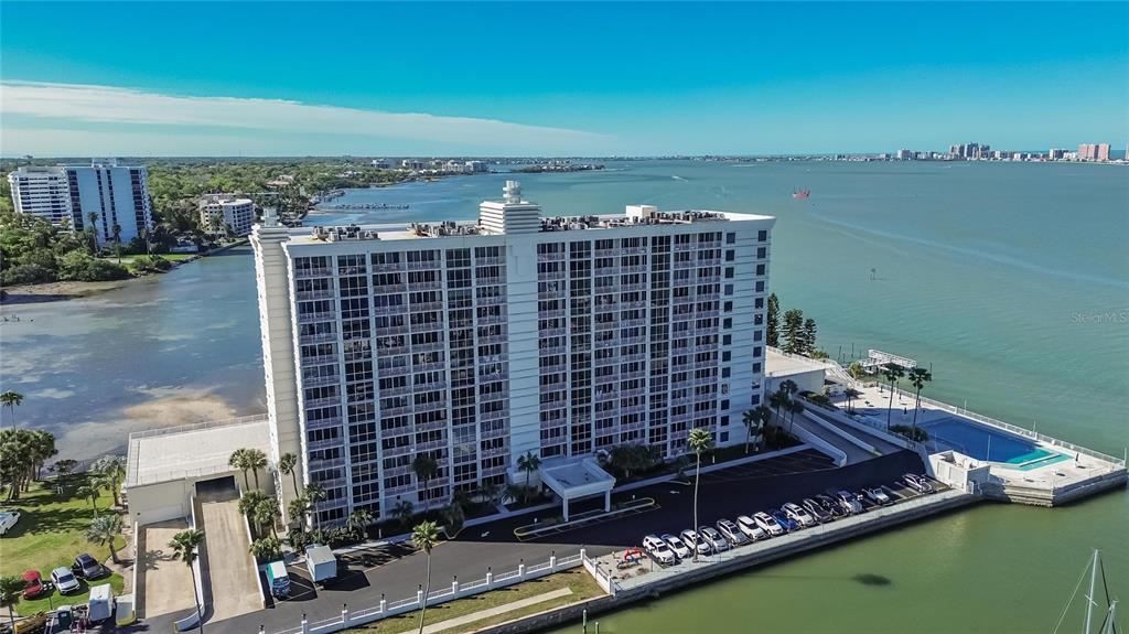 An aerial view shows a tall white residential building situated on a waterfront property — 100 PIERCE STREET UNIT 703, CLEARWATER, FL