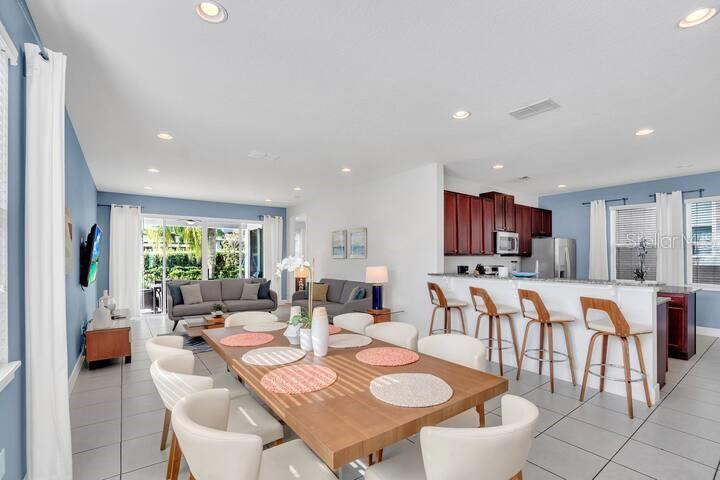 An open-concept dining area features a wooden table, white chairs, and a kitchen island — 200 PENDANT COURT, KISSIMMEE, FL