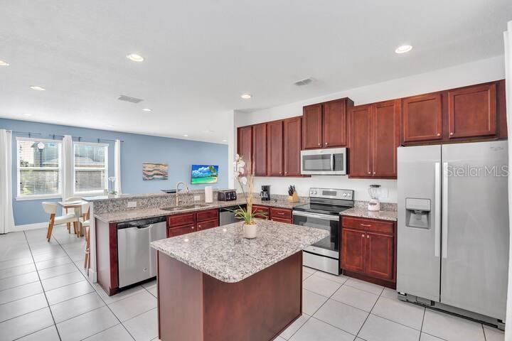 A kitchen features dark wood cabinets, granite countertops, stainless steel appliances, and a central island — 200 PENDANT COURT, KISSIMMEE, FL