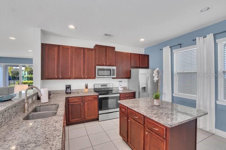 A kitchen features dark wood cabinets, granite countertops, stainless steel appliances, and a center island — 200 PENDANT COURT, KISSIMMEE, FL