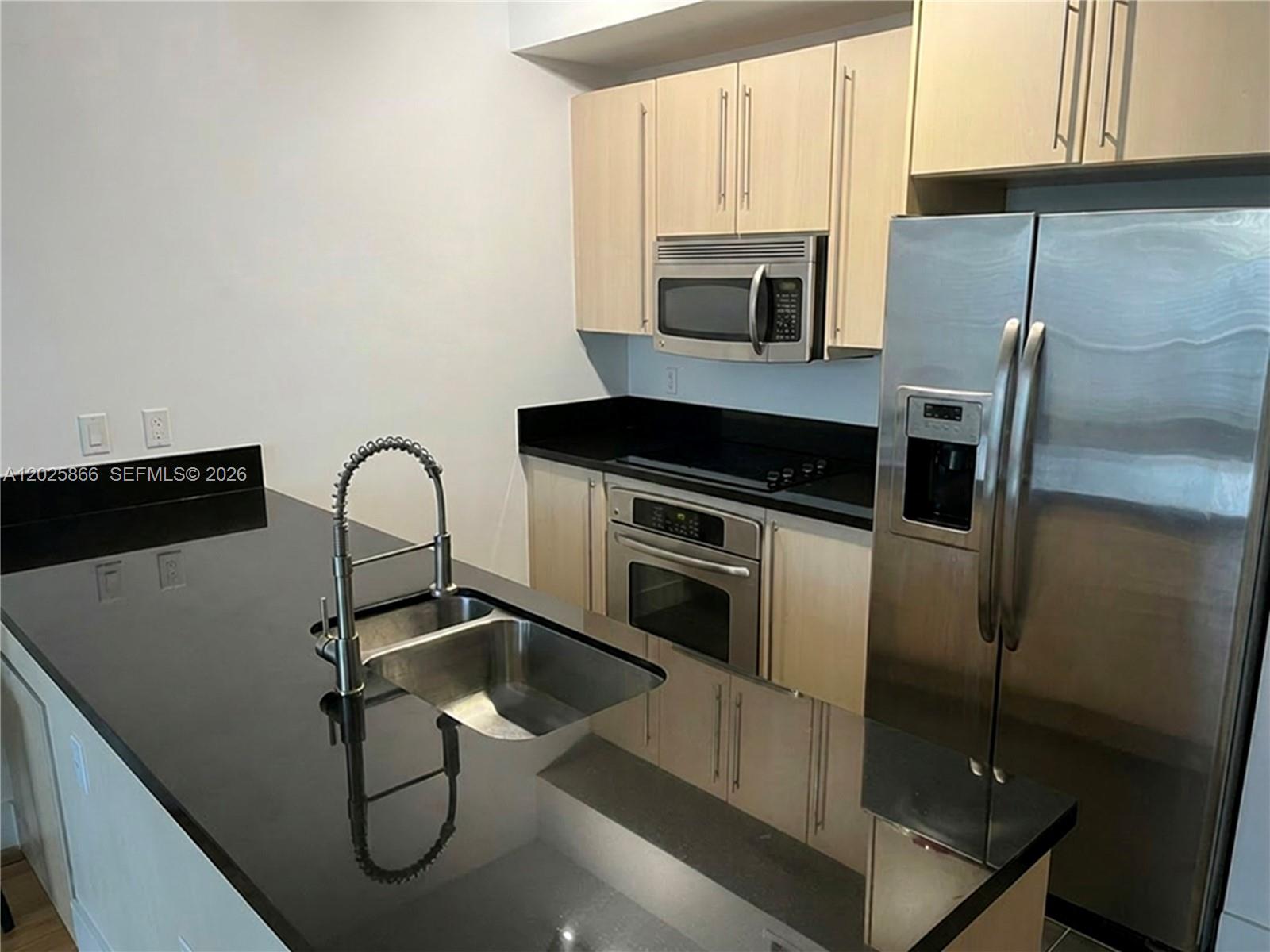 A kitchen features black countertops, stainless steel appliances, and light wood cabinetry — 79 SW 12 ST, Miami FL 33130, MIAMI, FL