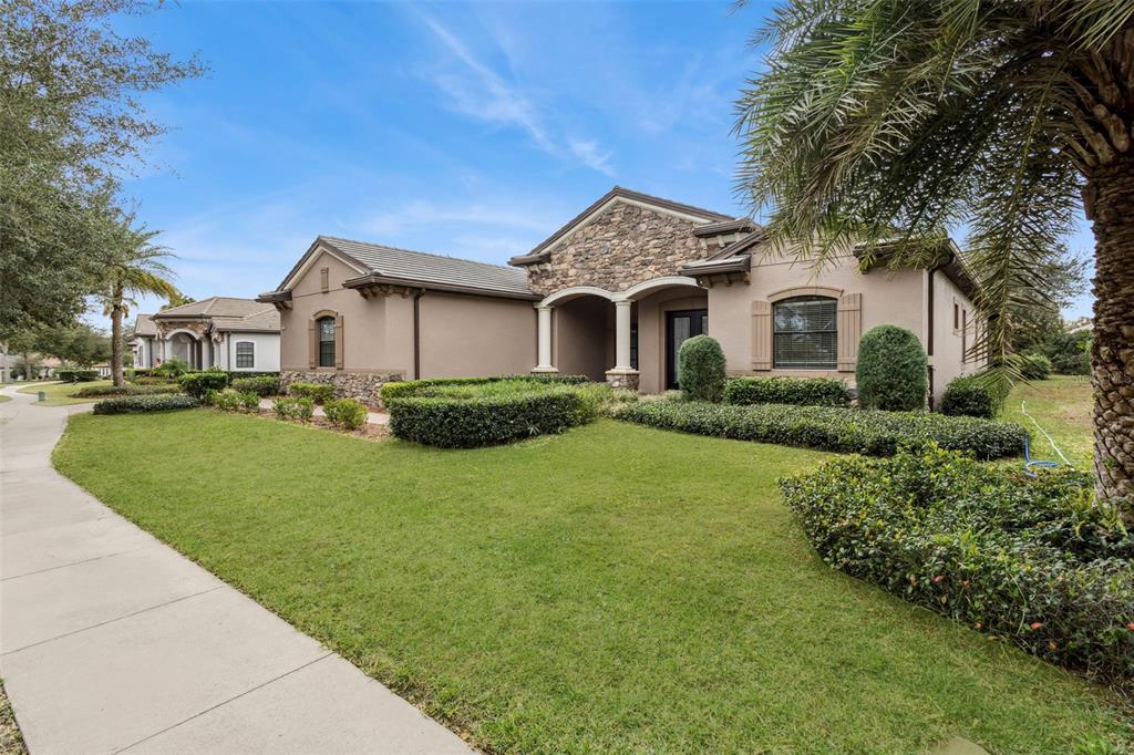 A single-story house with a stone facade, arched entryway, and manicured landscaping under a blue sky — 25499 HAWKS RUN LANE, SORRENTO, FL
