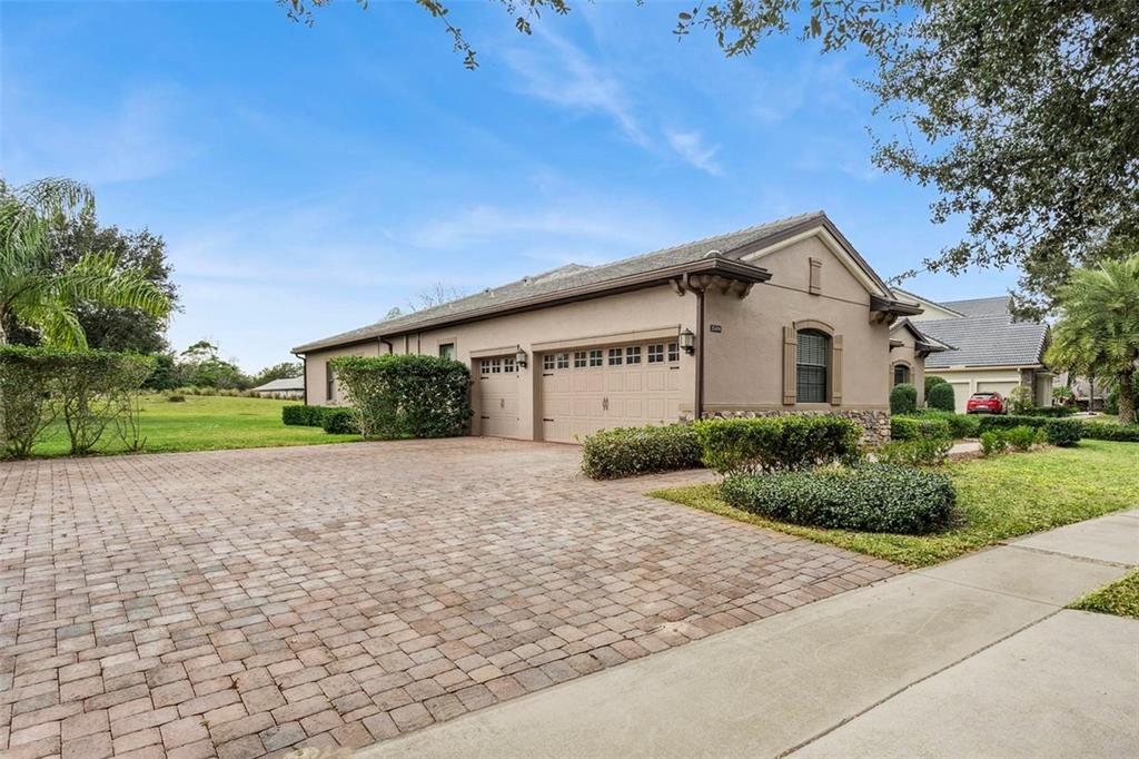 A tan single-story house with a brick paver driveway and a three-car garage — 25499 HAWKS RUN LANE, SORRENTO, FL