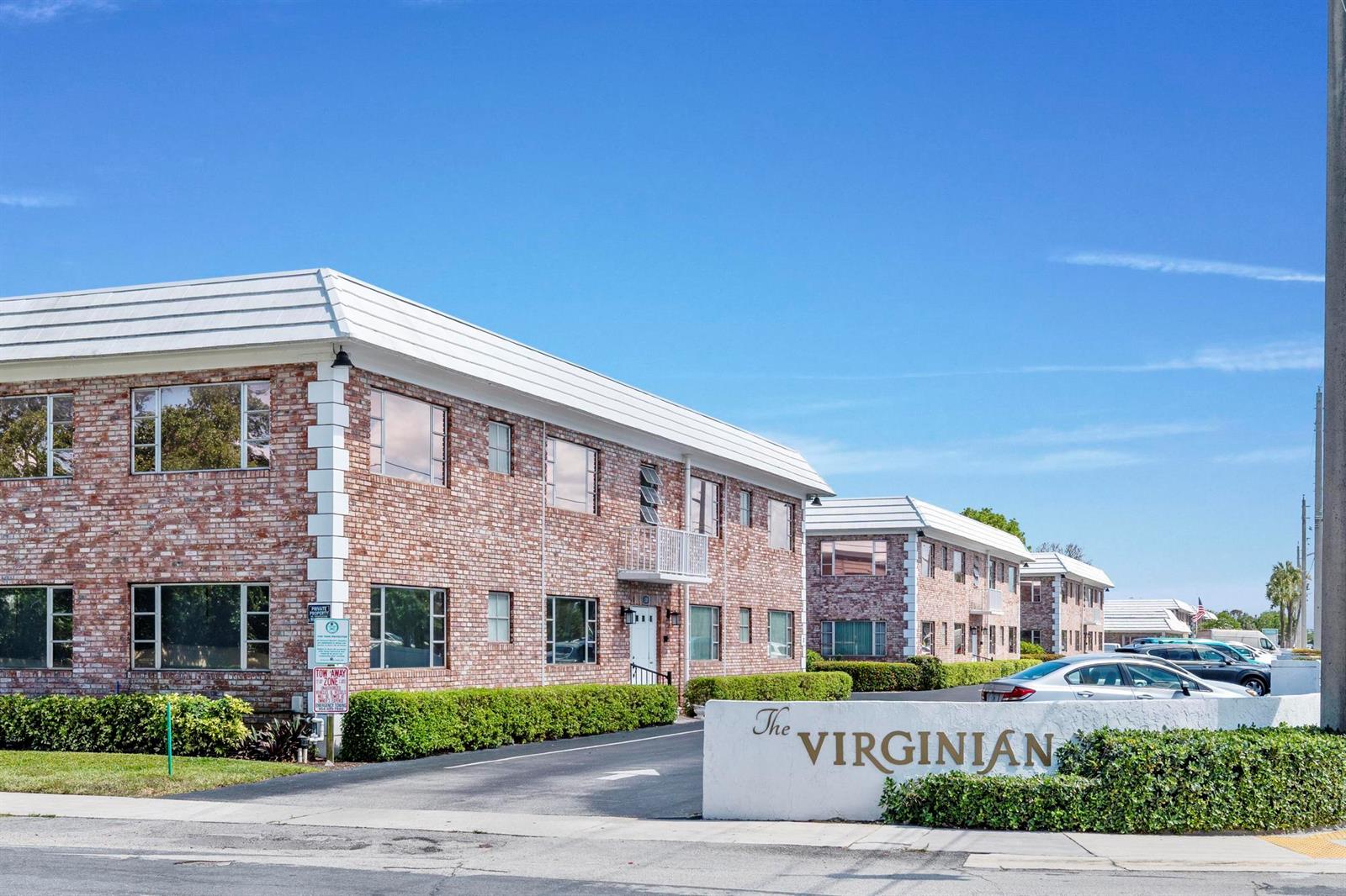 A multi-story brick apartment complex with a white roof and a sign reading The Virginian — 418 S Cypress Road # 128, Pompano Beach FL 33060, POMPANO BEACH, FL