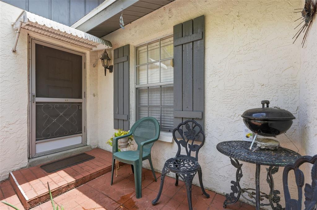 A patio features a brick floor, a screen door, a window with shutters, and furniture — 561 LAGUNA VISTA COURT, LARGO, FL