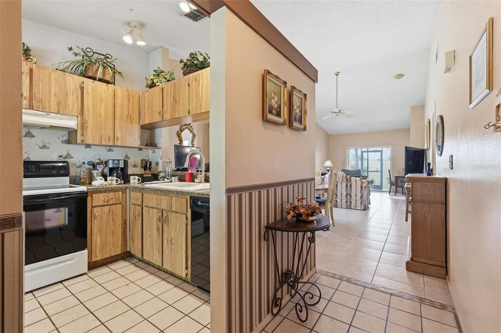 A kitchen with wood cabinets and tile floors opens into a living area with tile — 561 LAGUNA VISTA COURT, LARGO, FL