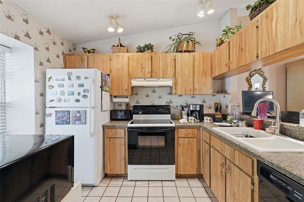A kitchen with light wood cabinets, white appliances, patterned wallpaper, and a tiled floor — 561 LAGUNA VISTA COURT, LARGO, FL