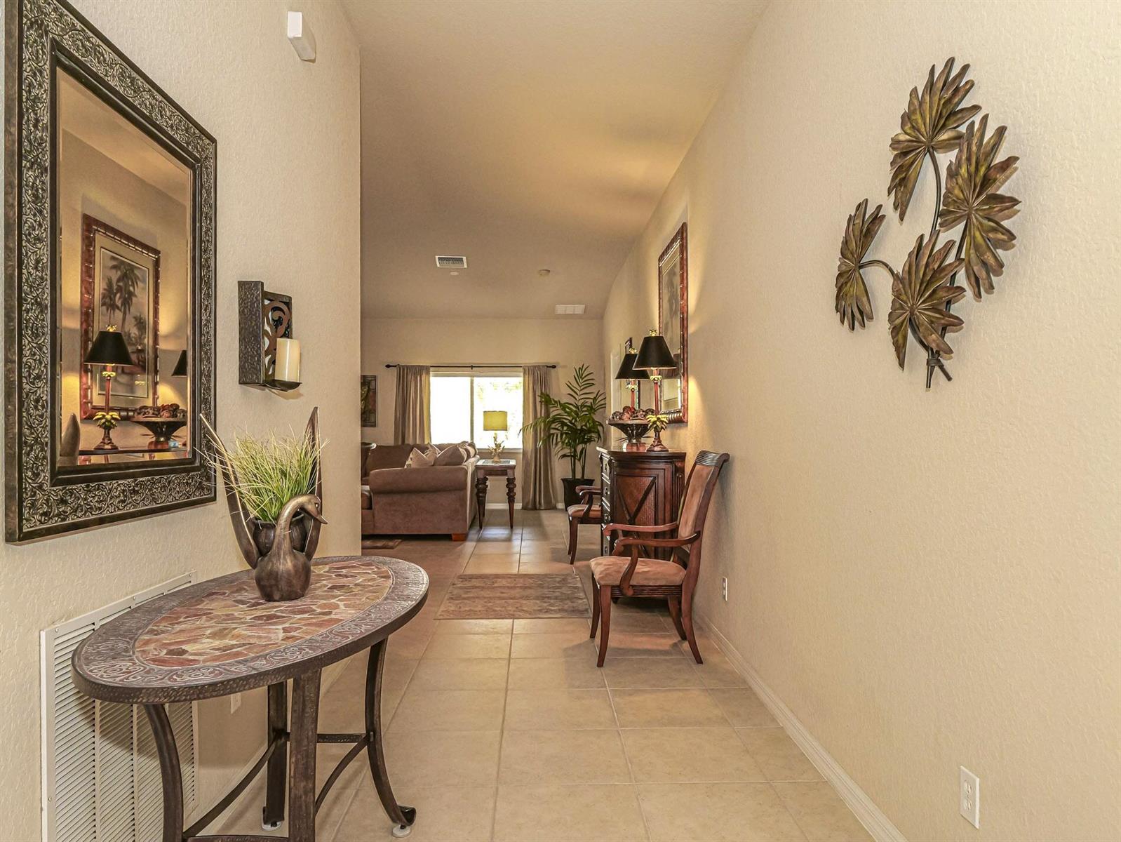 A tiled hallway leads to a living room with a console table and decorative wall art — 4528 56th Lane, Vero Beach FL 32967, VERO BEACH, FL